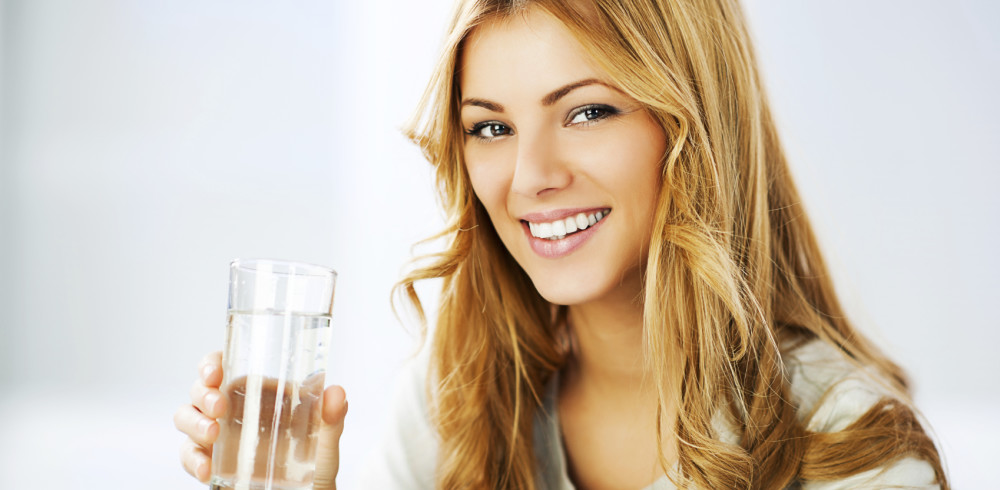 Smiling young woman holding glass with Purified Water and looking at the camera.