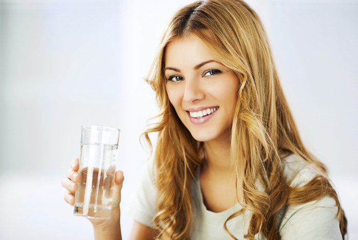 Smiling young woman holding glass with Purified Water and looking at the camera.